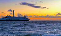 en smuk færge sejler på havet mellem Danmark og Tyskland. Der er en smuk solnedgang i baggrunden